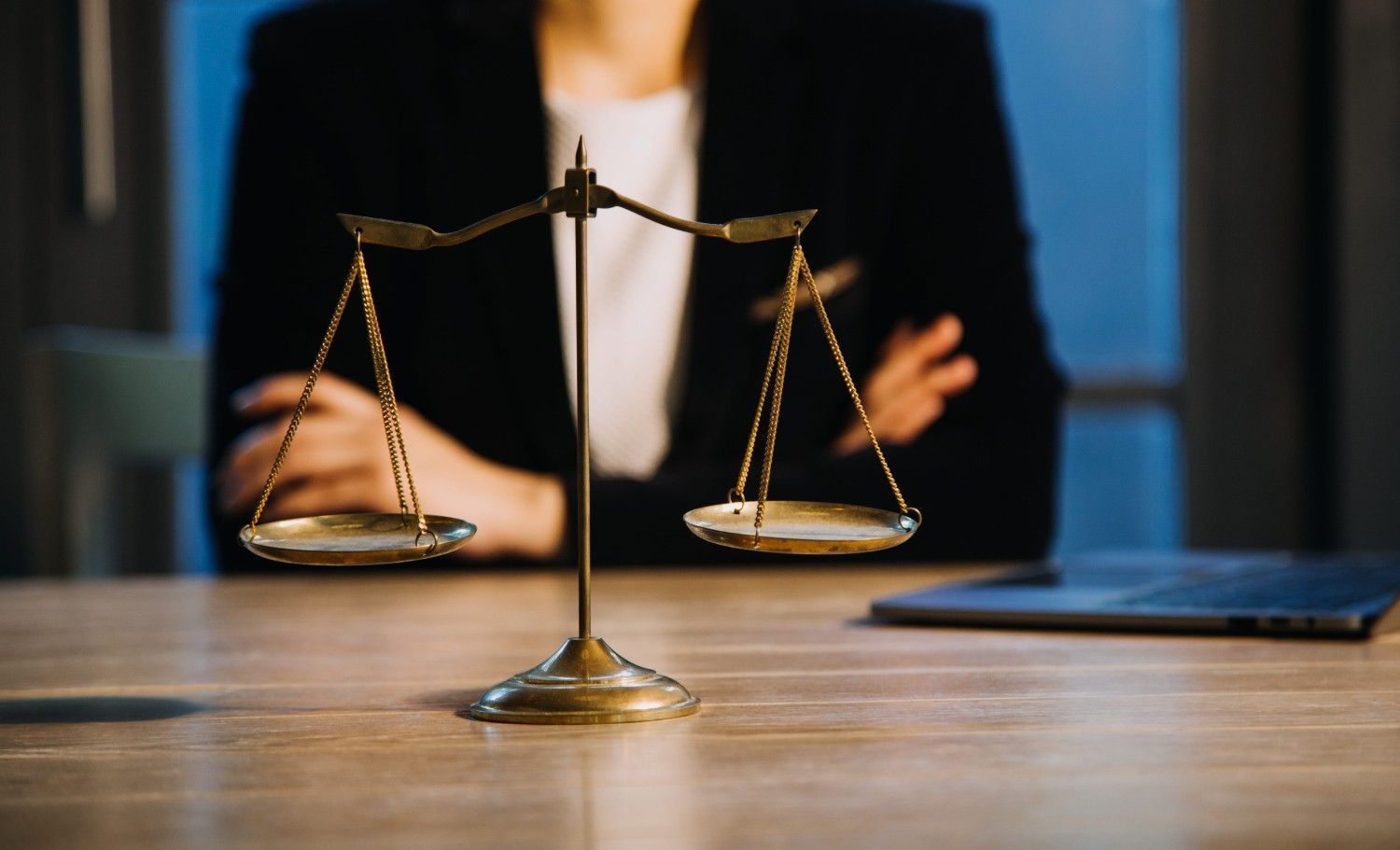 Una balanza de latón que representa la justicia reposa sobre un escritorio de madera frente a una persona.
