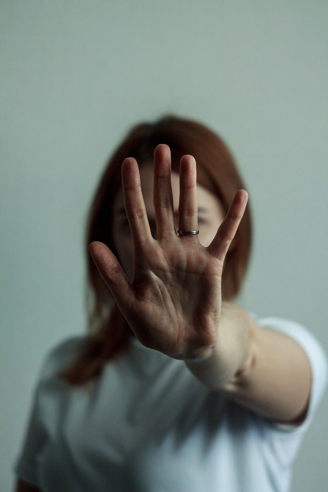 Una persona con cabello castaño rojizo lleva una camisa blanca y mantiene la mano levantada.