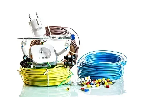 Cableado eléctrico y componentes, incluidos enchufes, cables y conectores, en paquetes de color amarillo, azul y marrón, sobre un fondo blanco.