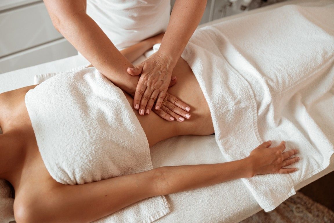Masaje de spa con manos que presionan la espalda de un hombre sobre una camilla de masaje blanca.