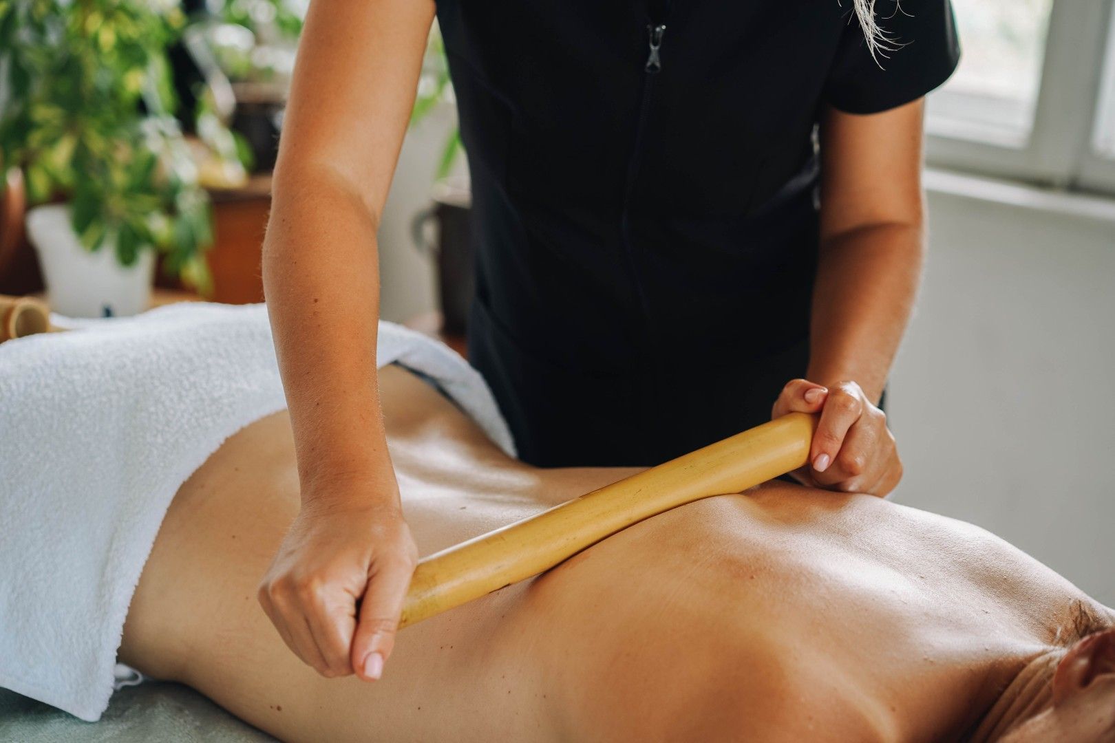 Masajista utilizando un rodillo de madera en la espalda desnuda de un cliente en un entorno de spa.