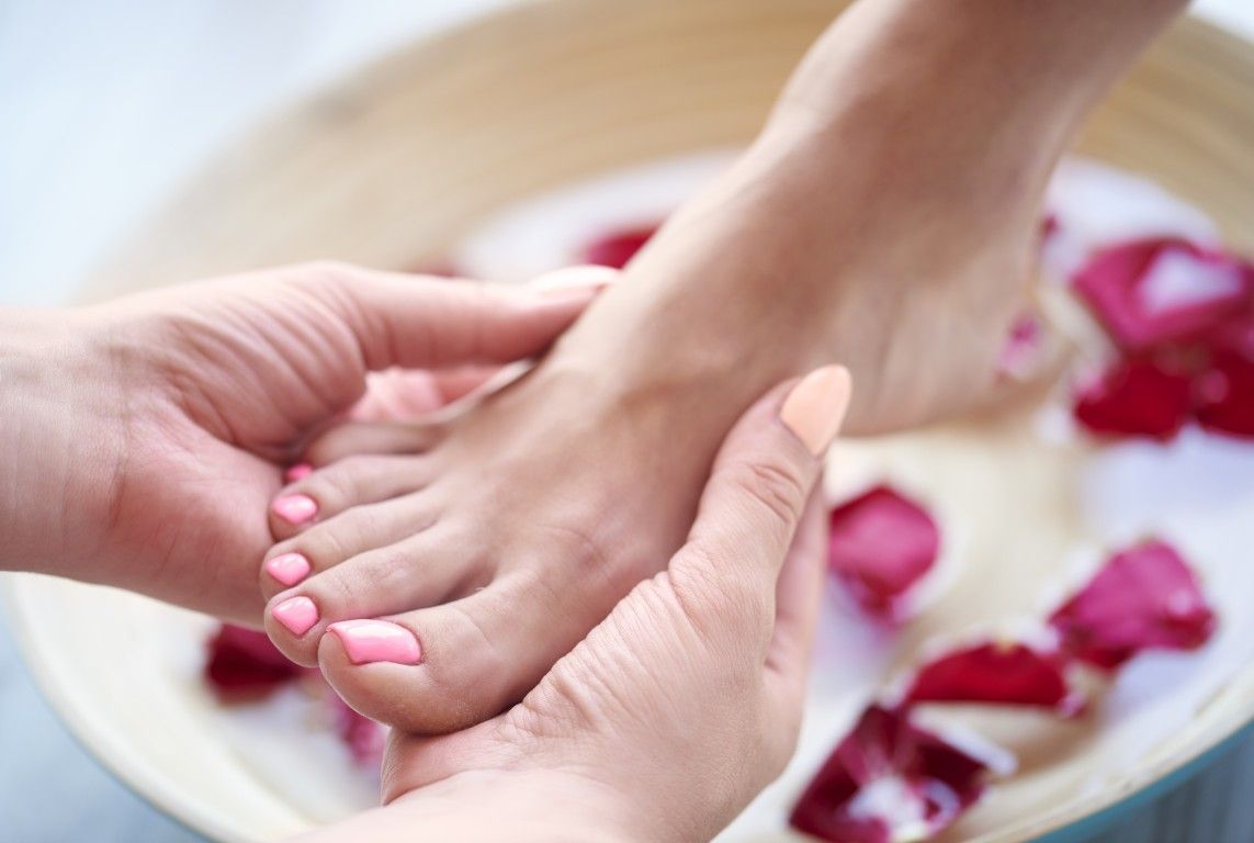 Pies sumergidos en un cuenco de madera con piedras blancas y espuma, que evocan un relajante baño de pies tipo spa.
