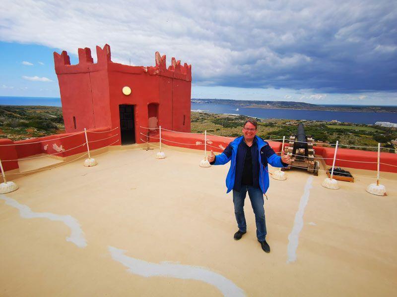 Ein Mann in einer blauen Jacke steht auf einem Dach vor einem roten Schloss.