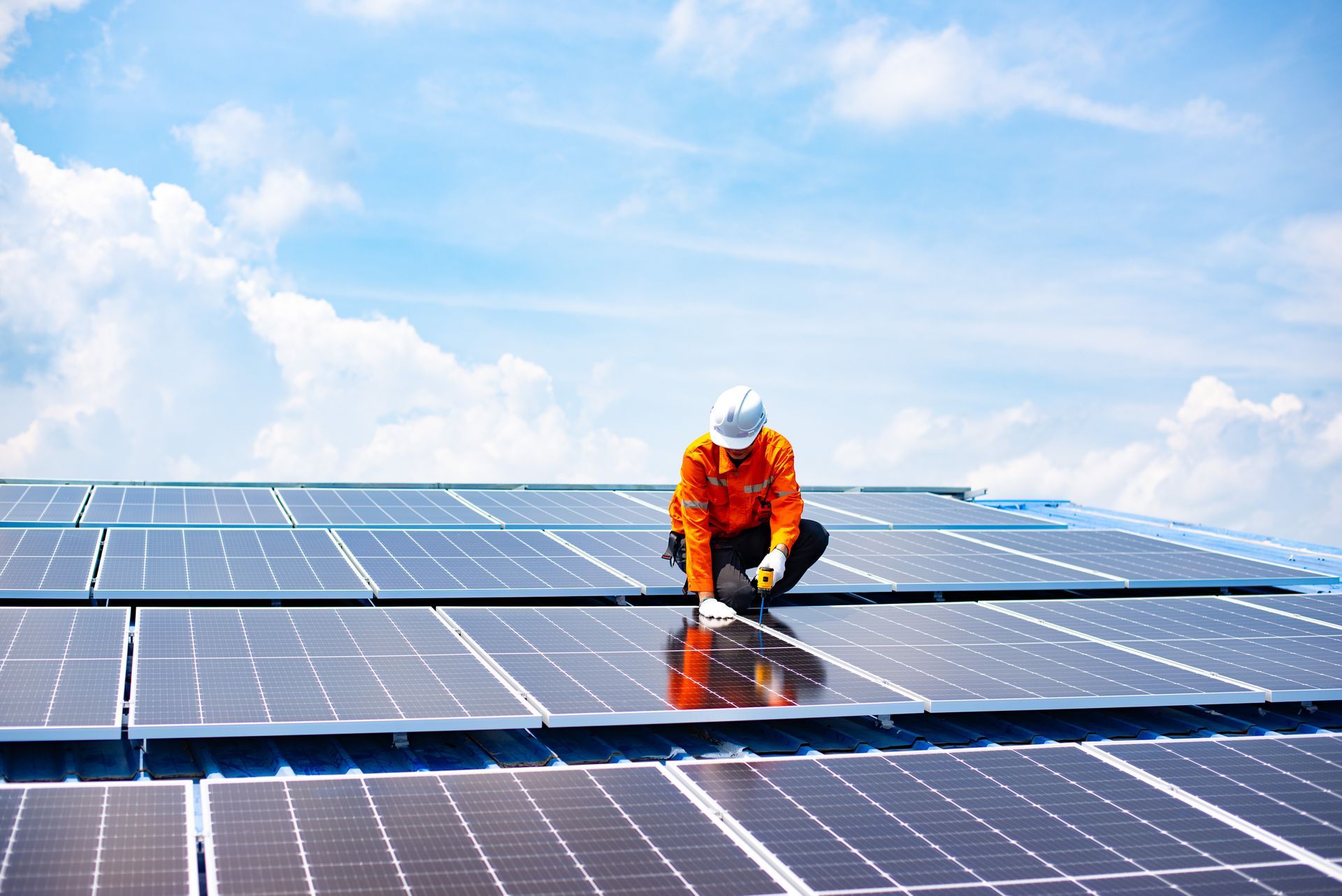 Ein Arbeiter in orangefarbener Schutzkleidung inspiziert Solarpaneele unter blauem Himmel