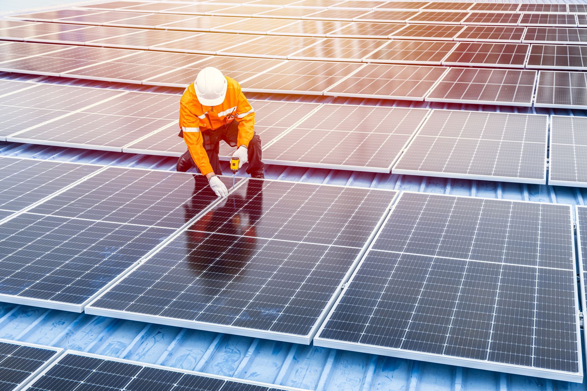Arbeiter in orangefarbener Schutzkleidung inspiziert Solarpaneele auf einem Dach