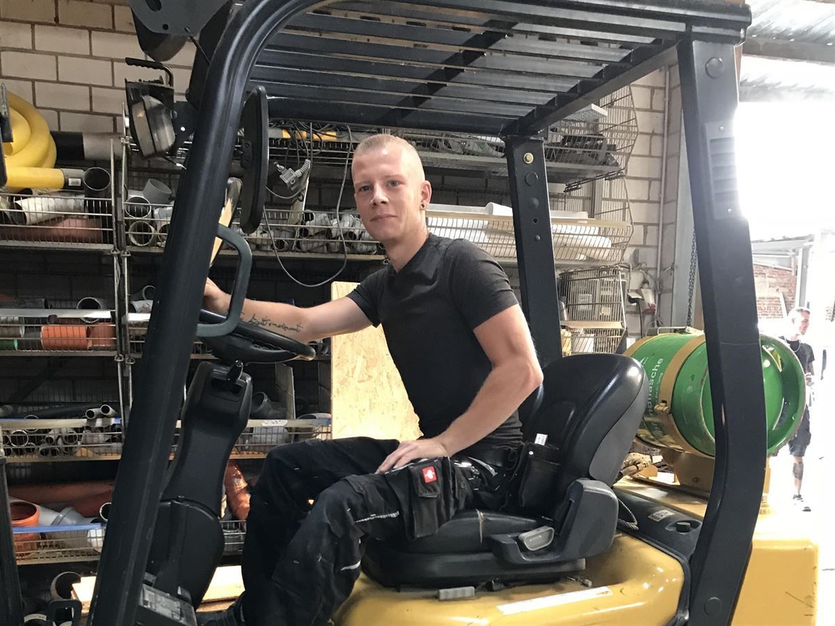 Ein Mann im schwarzen Hemd sitzt in einem Gabelstapler