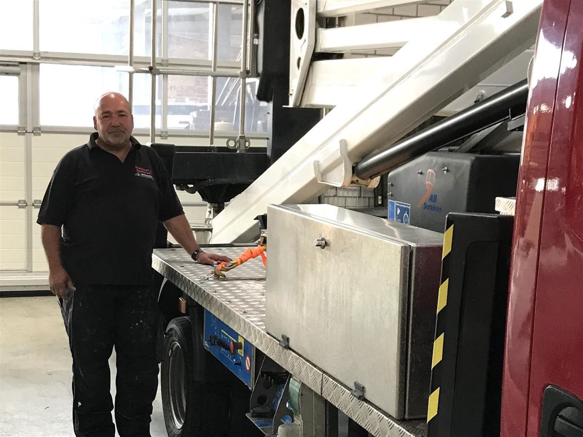 Ein Mann in einem schwarzen Hemd steht neben einer großen Maschine.