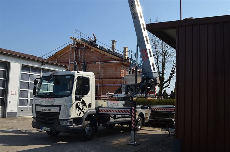 Ein weißer LKW mit einem Kran auf der Rückseite steht vor einem im Bau befindlichen Gebäude