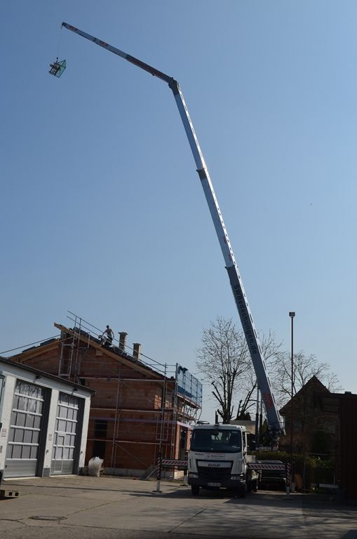 Ein LKW mit einem daran befestigten Kran steht vor einem im Bau befindlichen Gebäude.