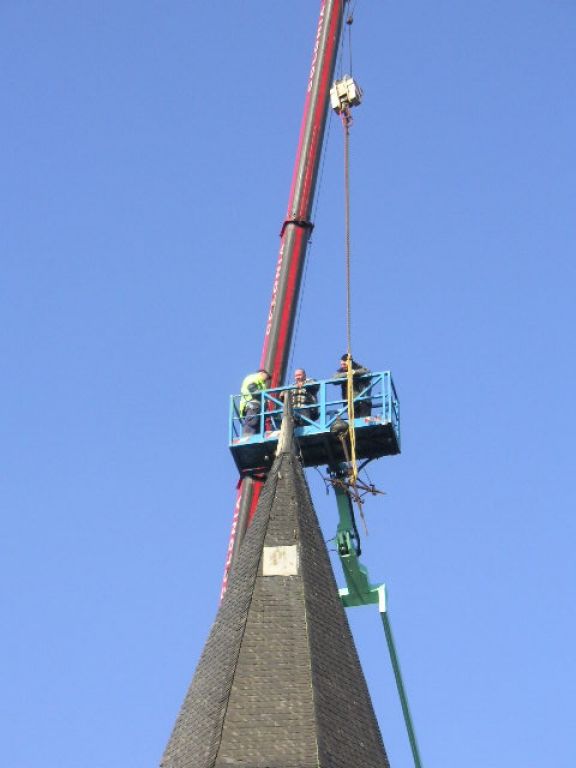 Ein Kran hebt eine Uhr auf die Spitze eines Kirchturms