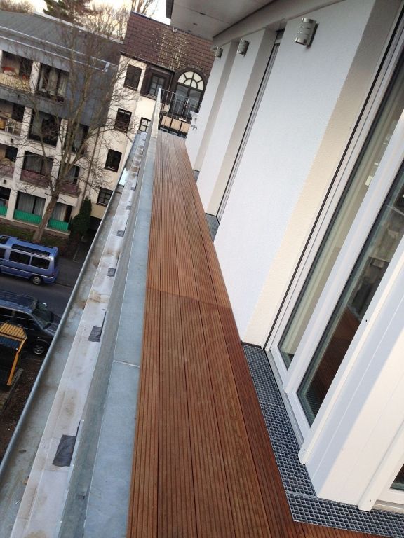 Ein Balkon mit Holzgeländer und einem weißen Gebäude im Hintergrund