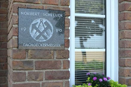 Ein Schild an einer Backsteinmauer mit der Aufschrift „Dachdeckermeister“