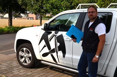 Ein Mann steht neben einem weißen Lastwagen und hält einen blauen Ordner in der Hand.