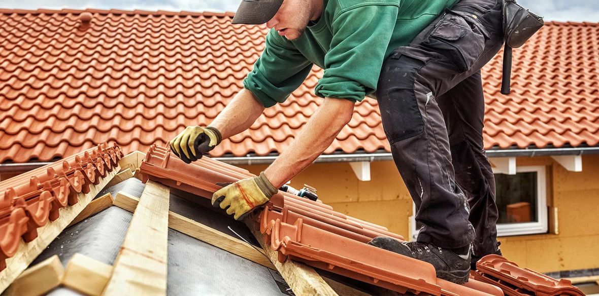 Ouvrier qualifié sur une toiture qui pose des tuiles neuves
