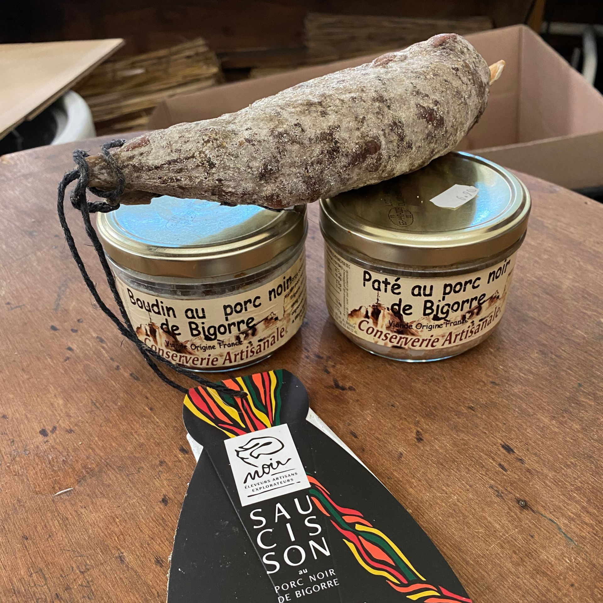 Un rouleau de salami et plusieurs tranches sur une planche à découper en bois, recouverts d'une nappe à carreaux rouges et blancs, sur une table rustique.