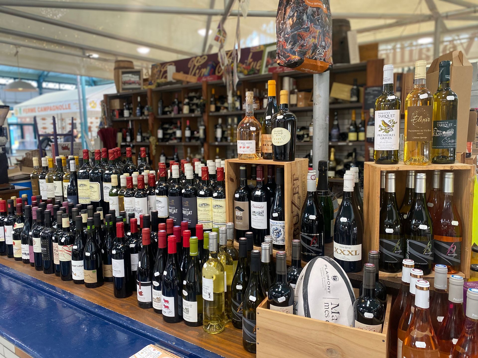 Des étagères remplies de nombreuses bouteilles de vin de couleurs et de marques variées sont exposées sur un marché.