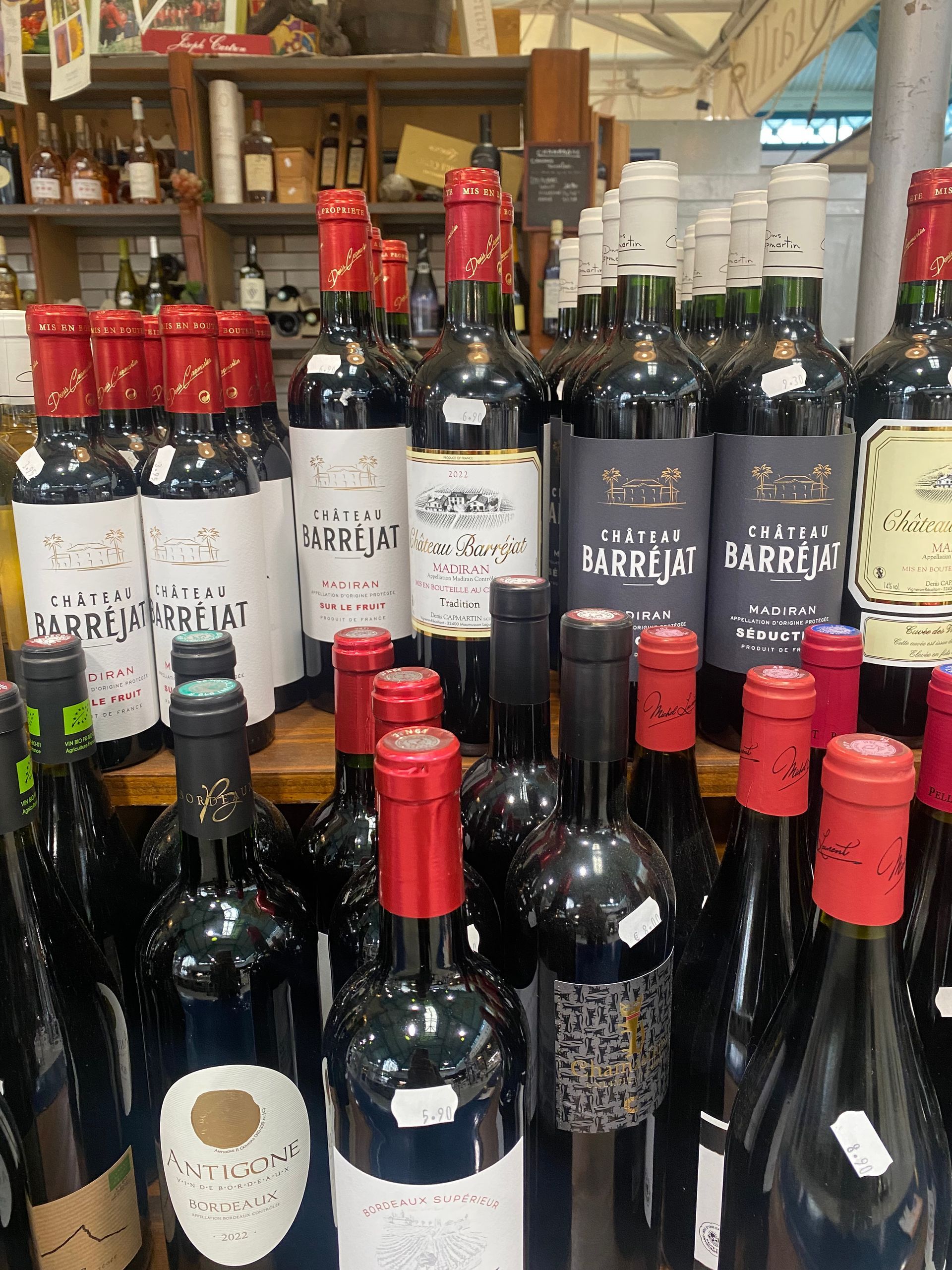 Un étalage de plusieurs bouteilles de vin avec capsules rouges et blanches sur les étagères d'un magasin.