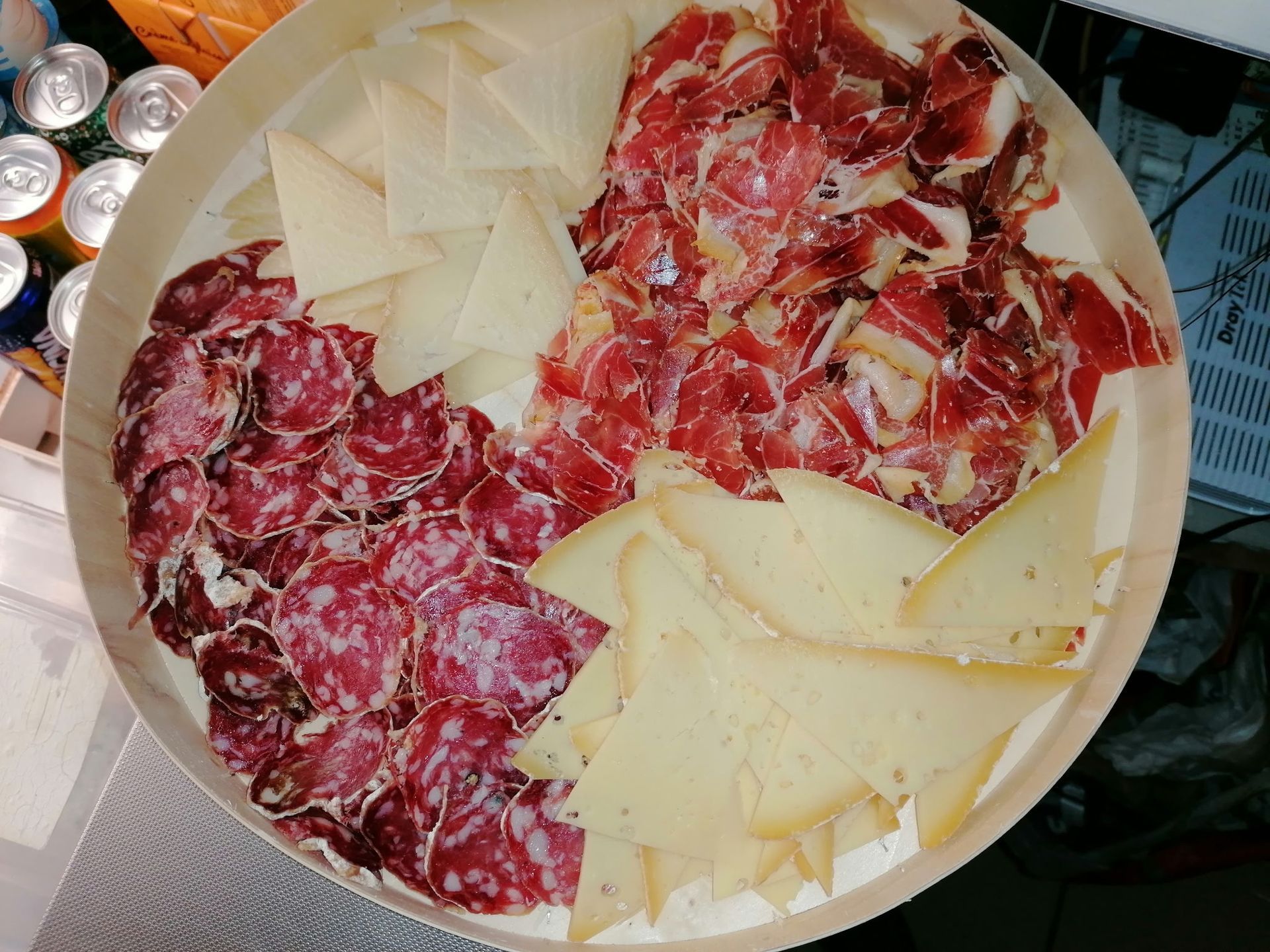Un plateau de charcuterie rond composé de tranches de salami, de prosciutto et de morceaux triangulaires de fromages à pâte dure.