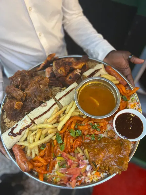 A man is holding a plate of food with french fries and sauce.