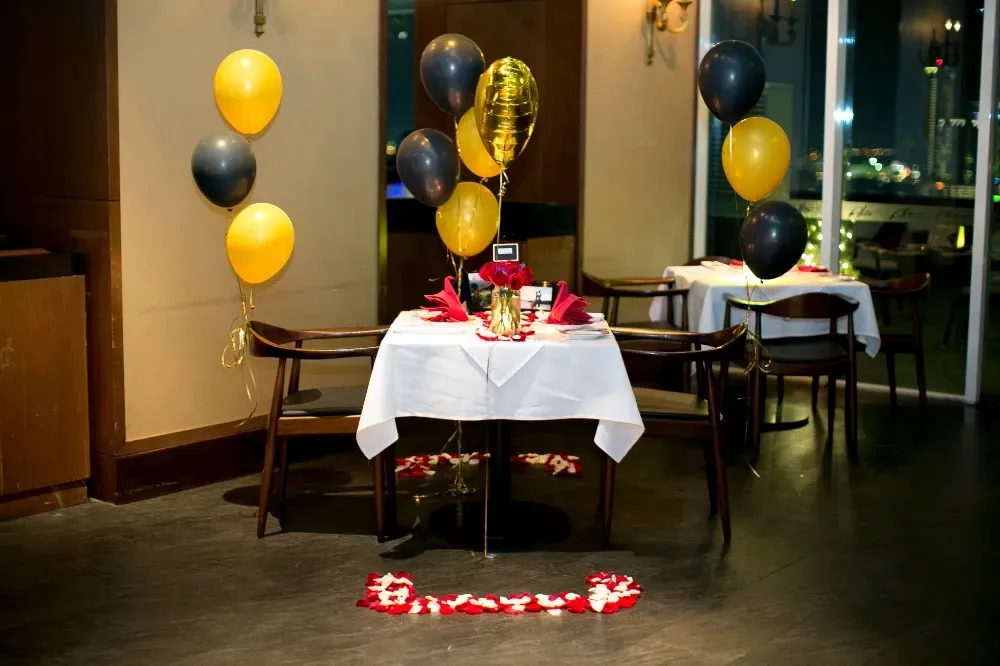A restaurant with a table and chairs decorated with balloons and rose petals.