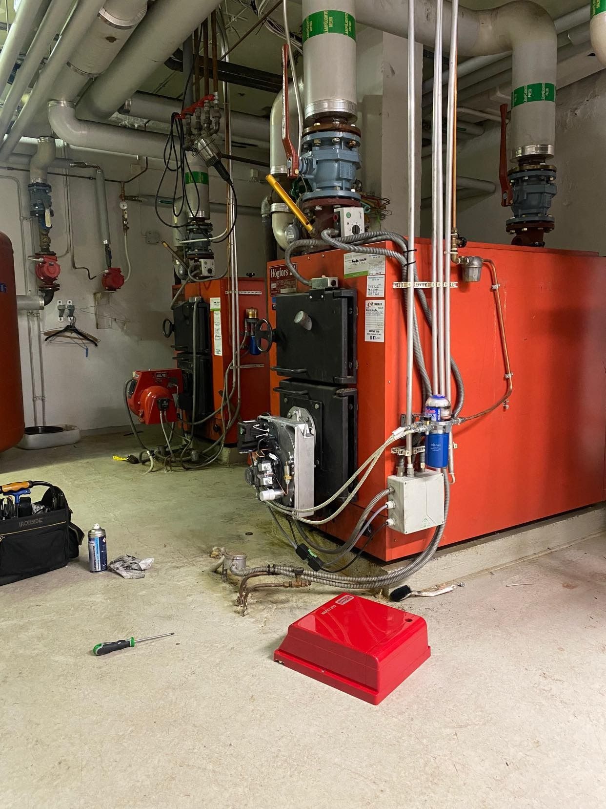 Punaisia teollisuuskattiloita mekaanisessa huoneessa, putkineen ja laitteineen.