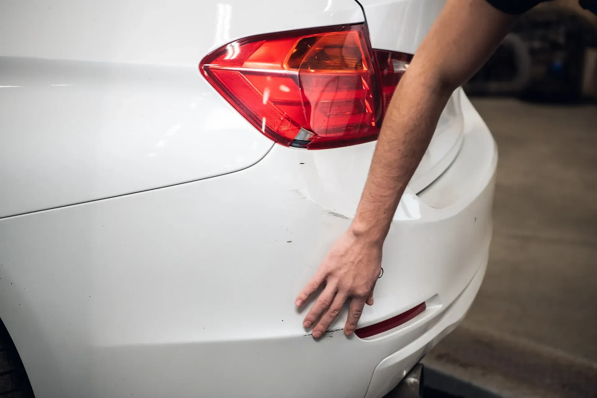 Mano revisando el parachoques trasero blanco de un automóvil para ver si tiene daños.