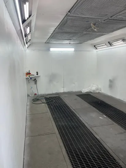 Vista interior de una cabina de pintura en aerosol , con una rejilla de piso, luces superiores y una estación de trabajo.