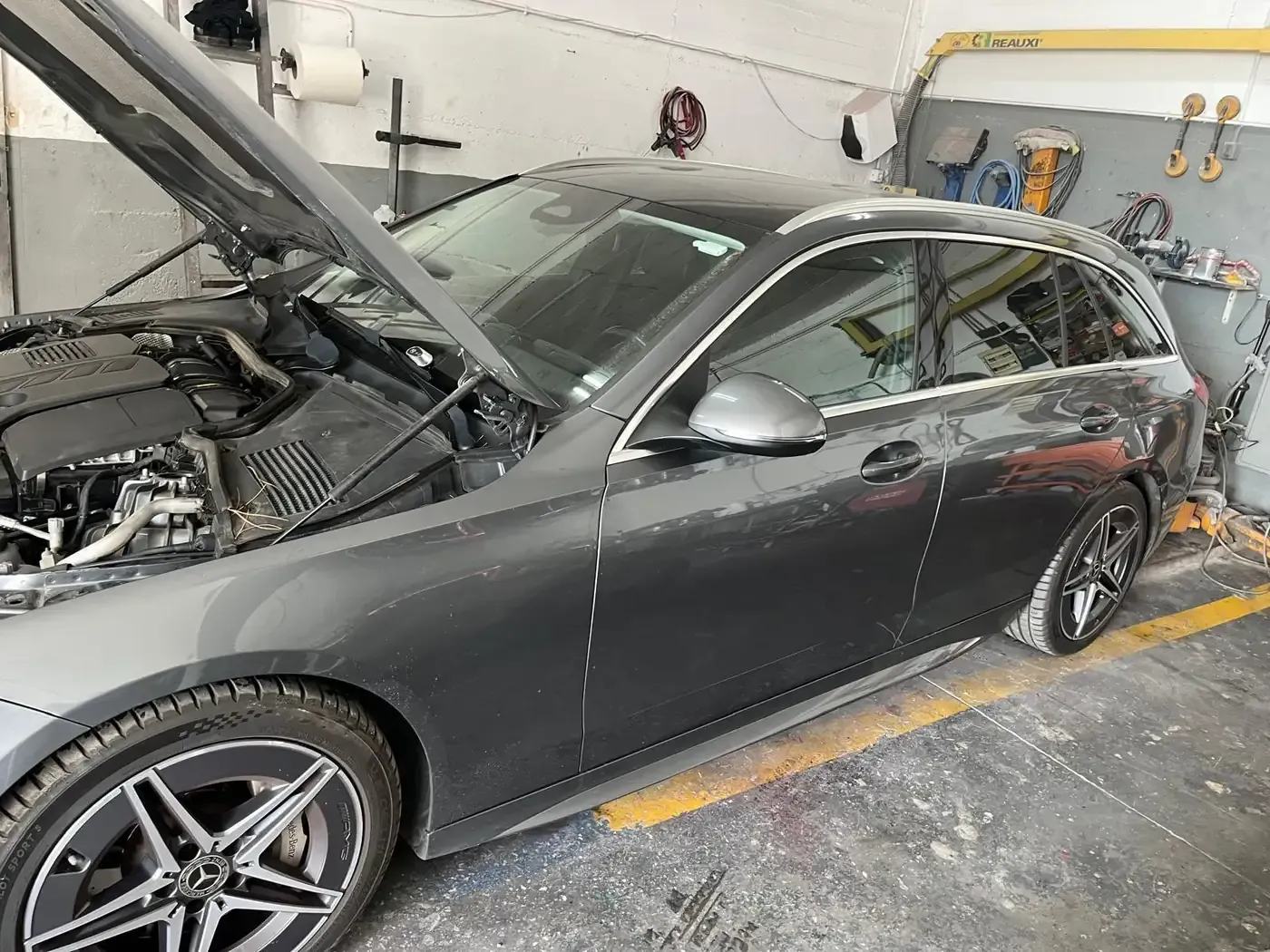 Una camioneta Mercedes-Benz de color gris con el capó abierto en un garaje, probablemente para reparaciones.