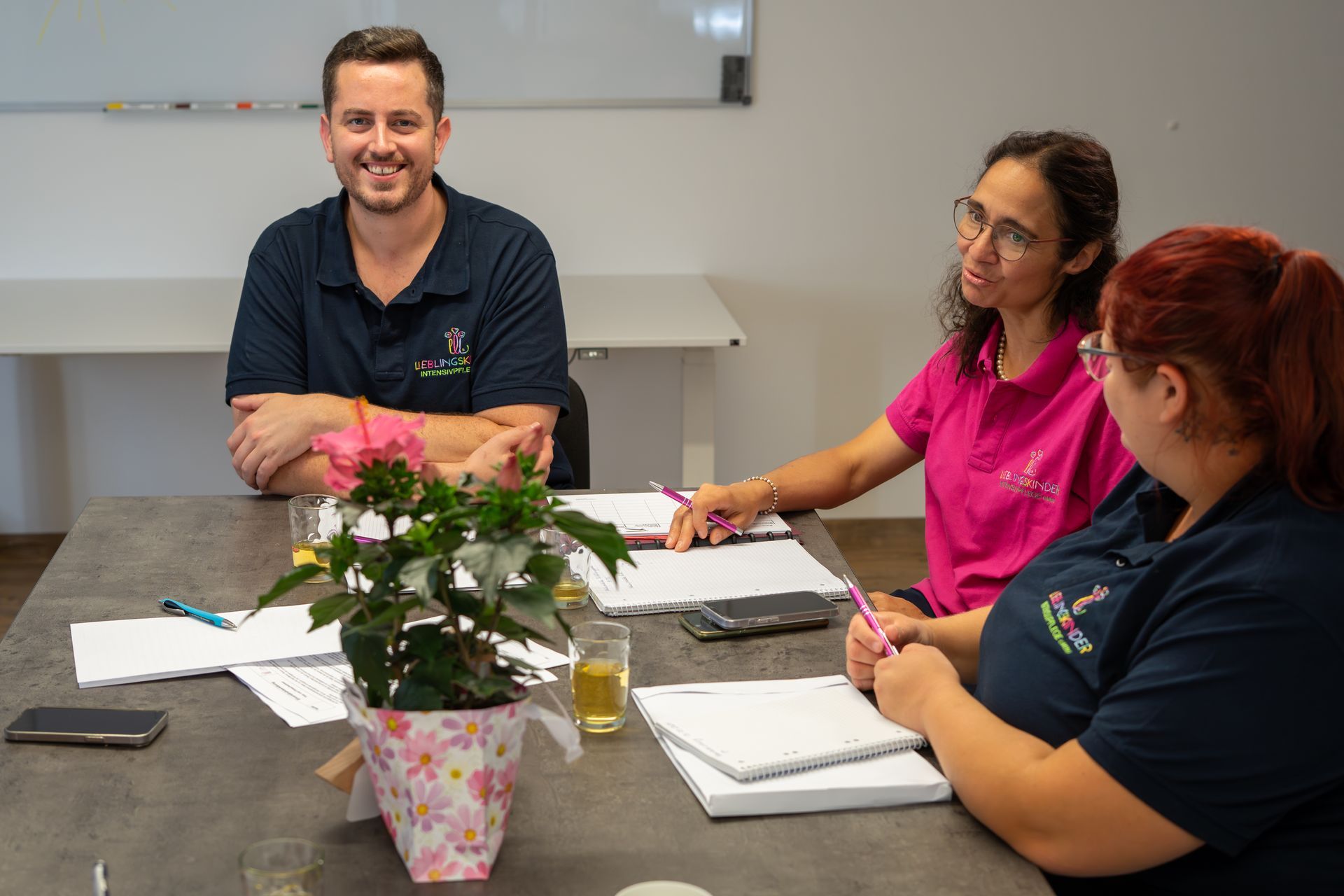 Kleine Kinder spielen unter Aufsicht eines Erwachsenen in einem hell erleuchteten Raum mit Bauklötzen an einem Tisch.