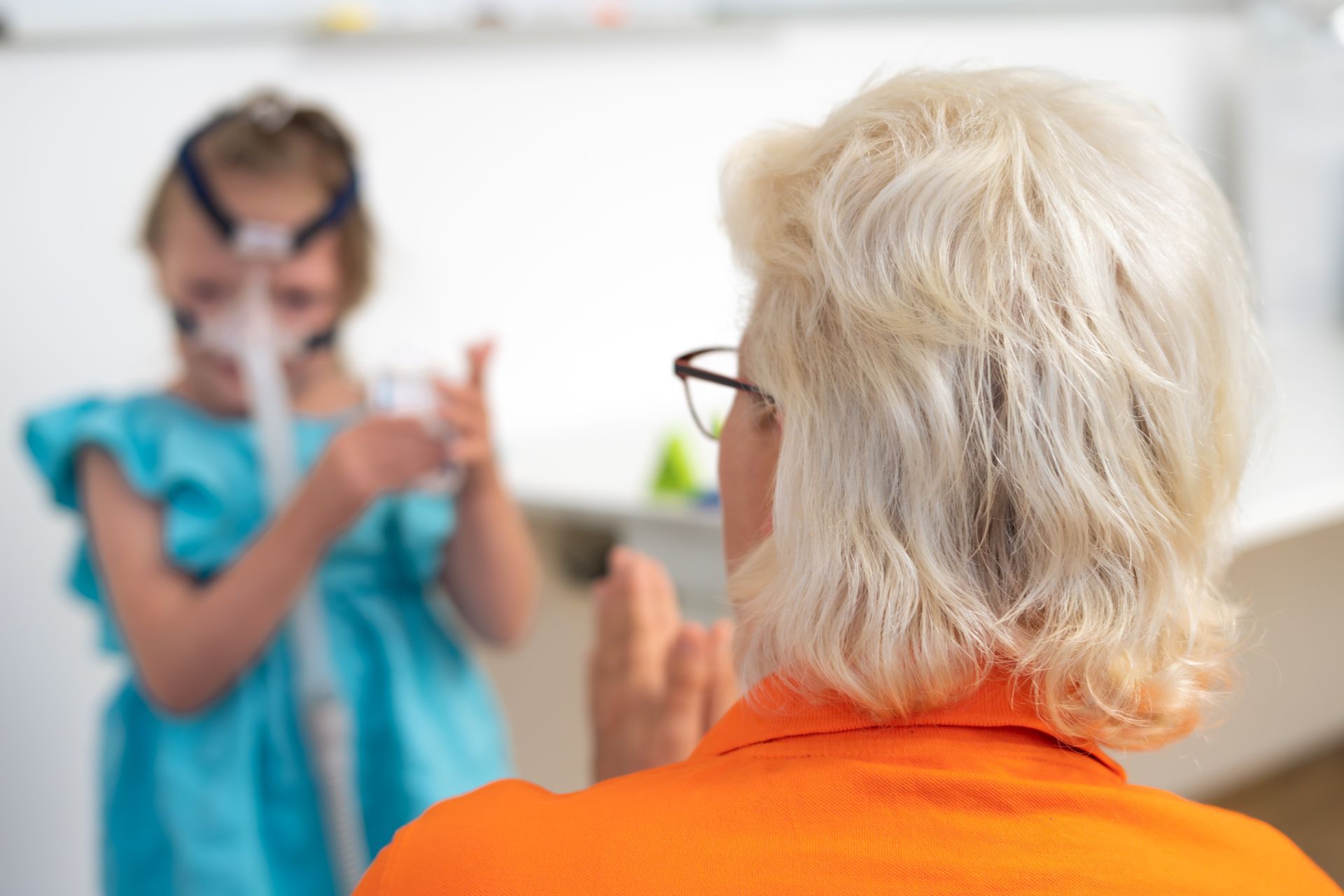 Eine Krankenschwester hilft einem Kind bei der Anwendung eines Verneblers. Beide lächeln drinnen.