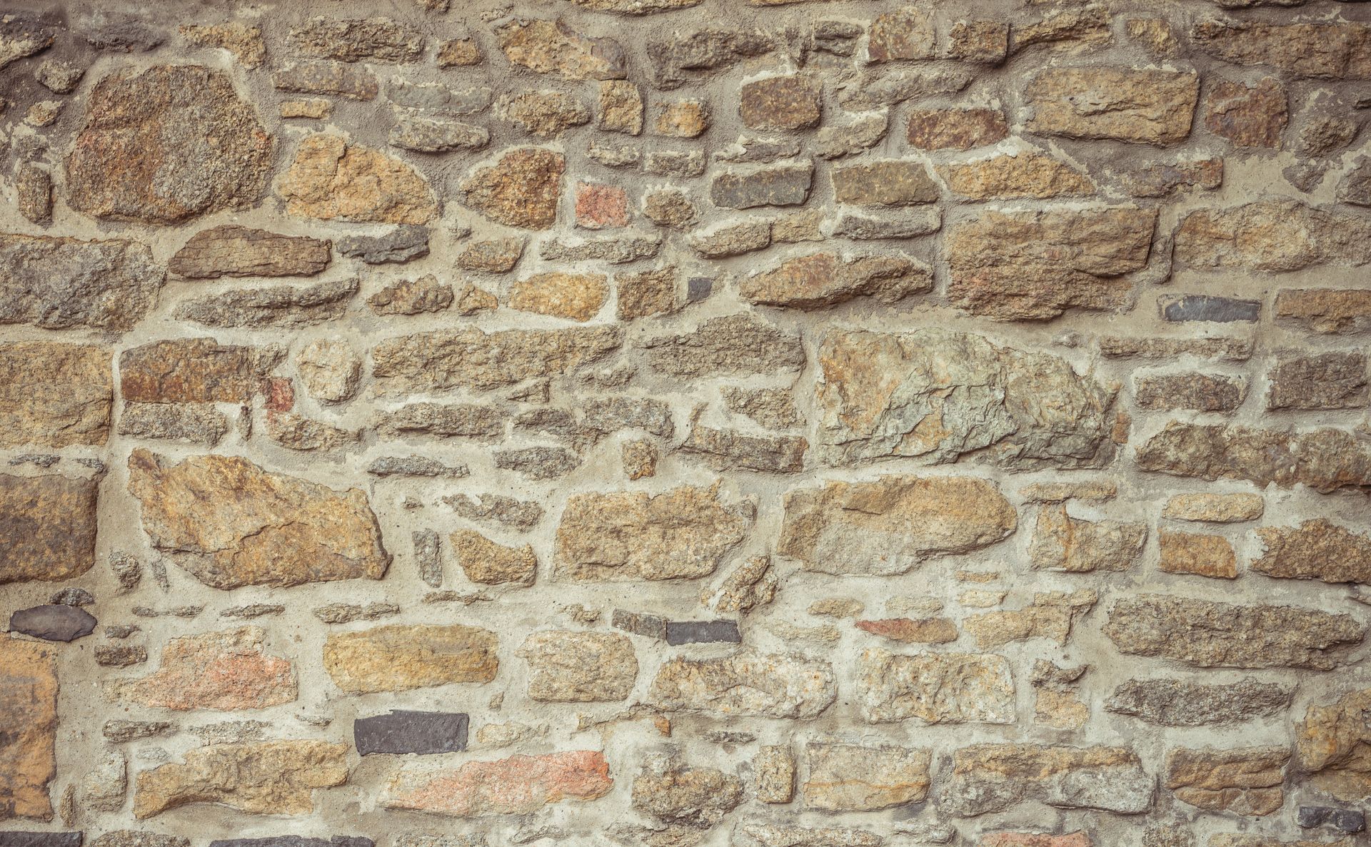 Un mur construit avec des pierres de forme irrégulière, de couleur beige et grise, à la texture variée, maintenues ensemble par du mortier.