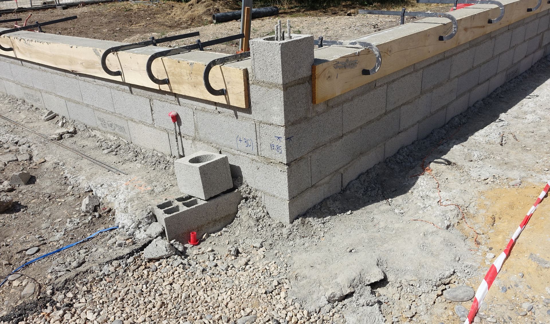 Un mur de pierre construit avec des blocs irréguliers, sombres et gris, agrémenté de touffes de lierre vert poussant à sa surface.