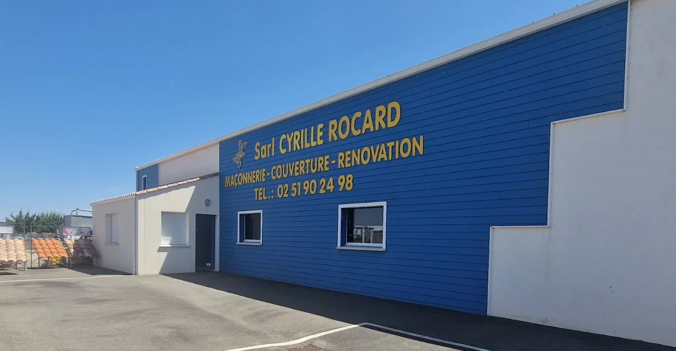 Un immeuble commercial bleu et blanc arborant une enseigne dorée pour SARL Cyrille Rocard, sous un ciel bleu azur.