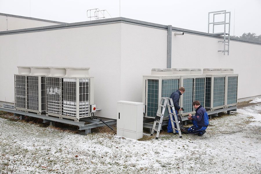 Zwei Männer arbeiten außerhalb eines Gebäudes an einer großen Klimaanlage.