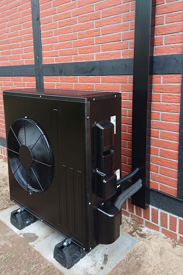 Neben einer Backsteinmauer steht eine schwarze Klimaanlage.