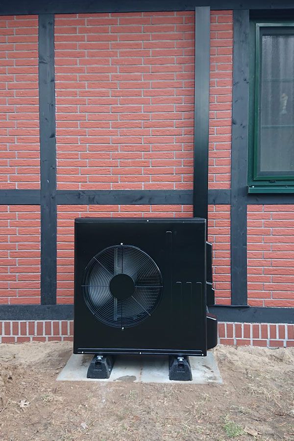 Eine schwarze Klimaanlage steht außerhalb eines Backsteingebäudes.