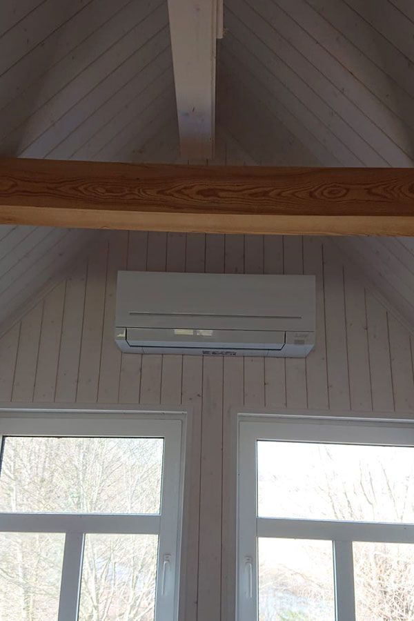 In einem Raum mit zwei Fenstern hängt eine weiße Klimaanlage von der Decke.