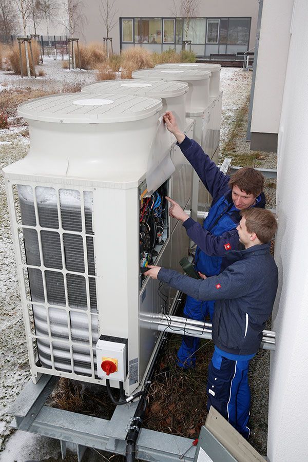 Zwei Männer arbeiten außerhalb eines Gebäudes an einer großen Klimaanlage.
