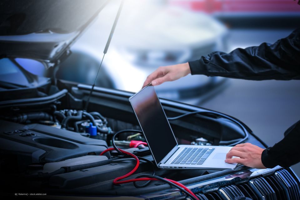 Person mit Notebook untersucht Motorhaube