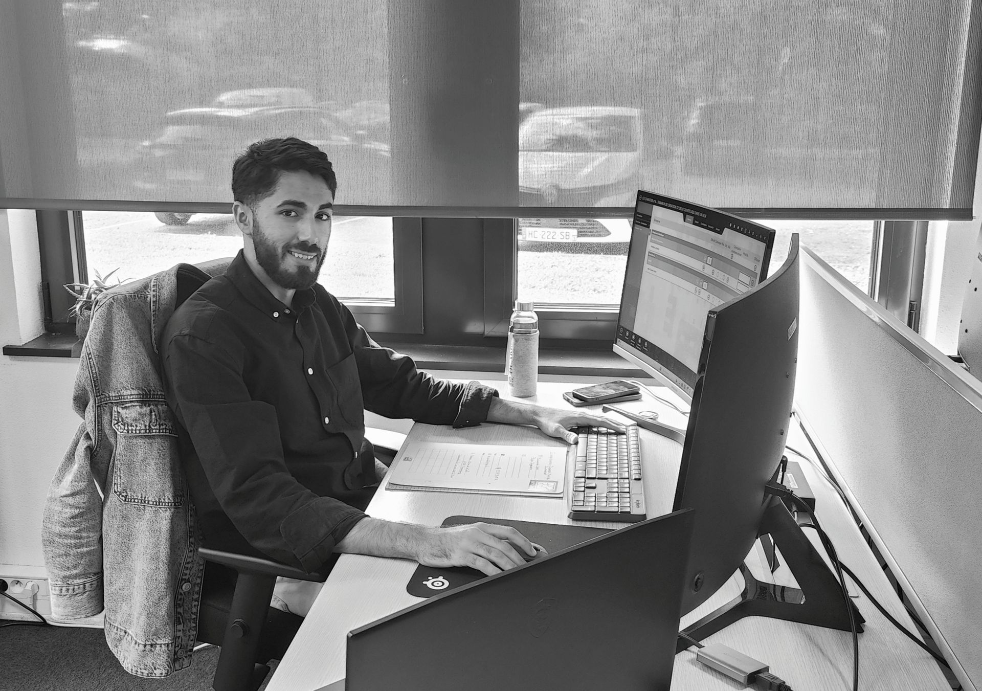 Hichem Aoufi assis à son bureau, souriant devant son ordinateur.