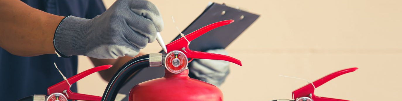 Personne inspectant un extincteur, portant des gants et tenant un presse-papiers.