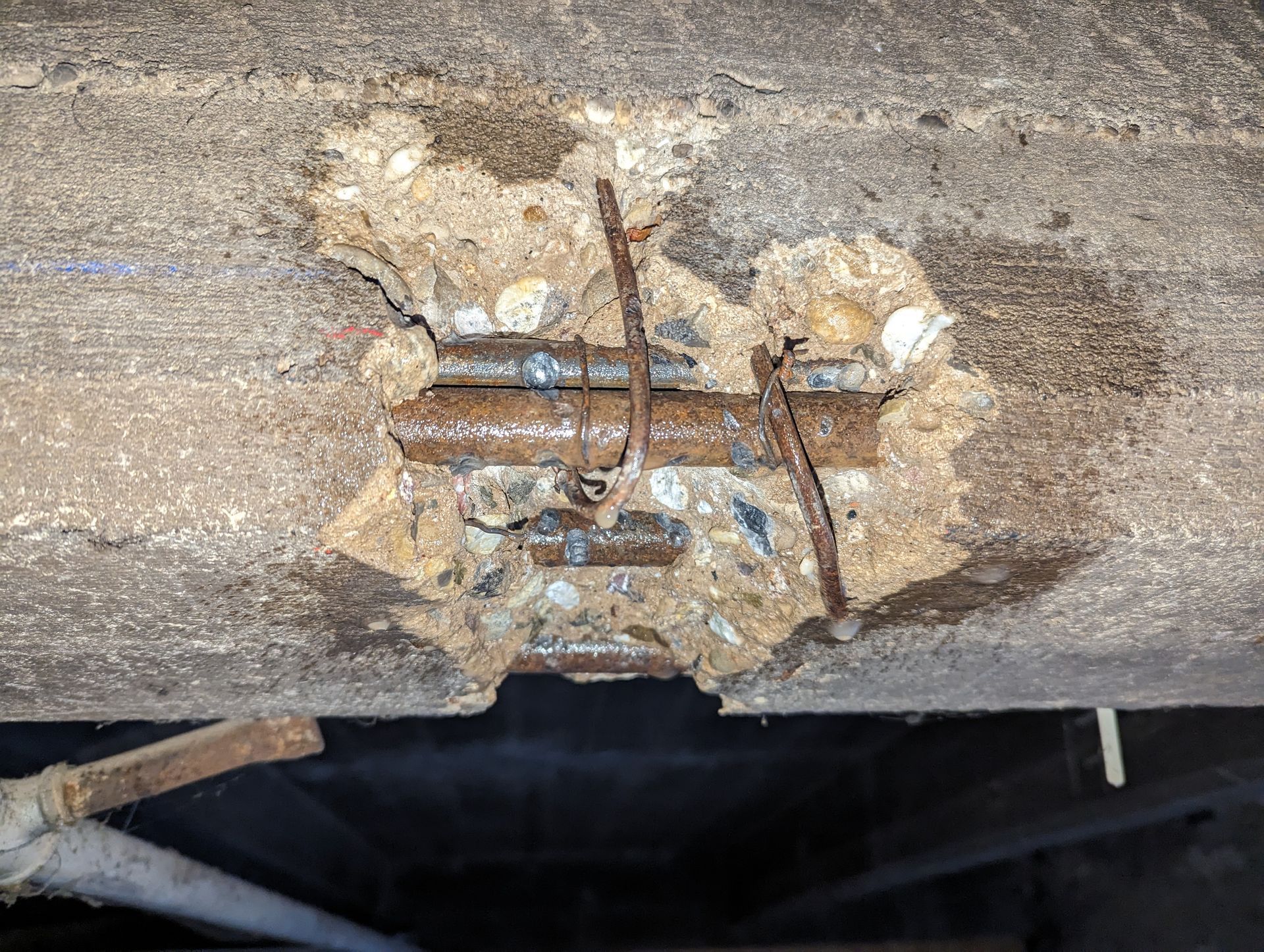 Poutre en béton avec zone endommagée exposant des barres d'armature rouillées.