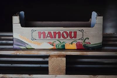 Caja de cartón de la marca Nanou sobre un estante de madera, con coloridos dibujos de frutas y laterales grises.