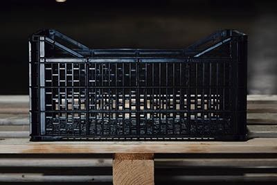 Caja de plástico negra sobre un palé de madera en un entorno de almacén.