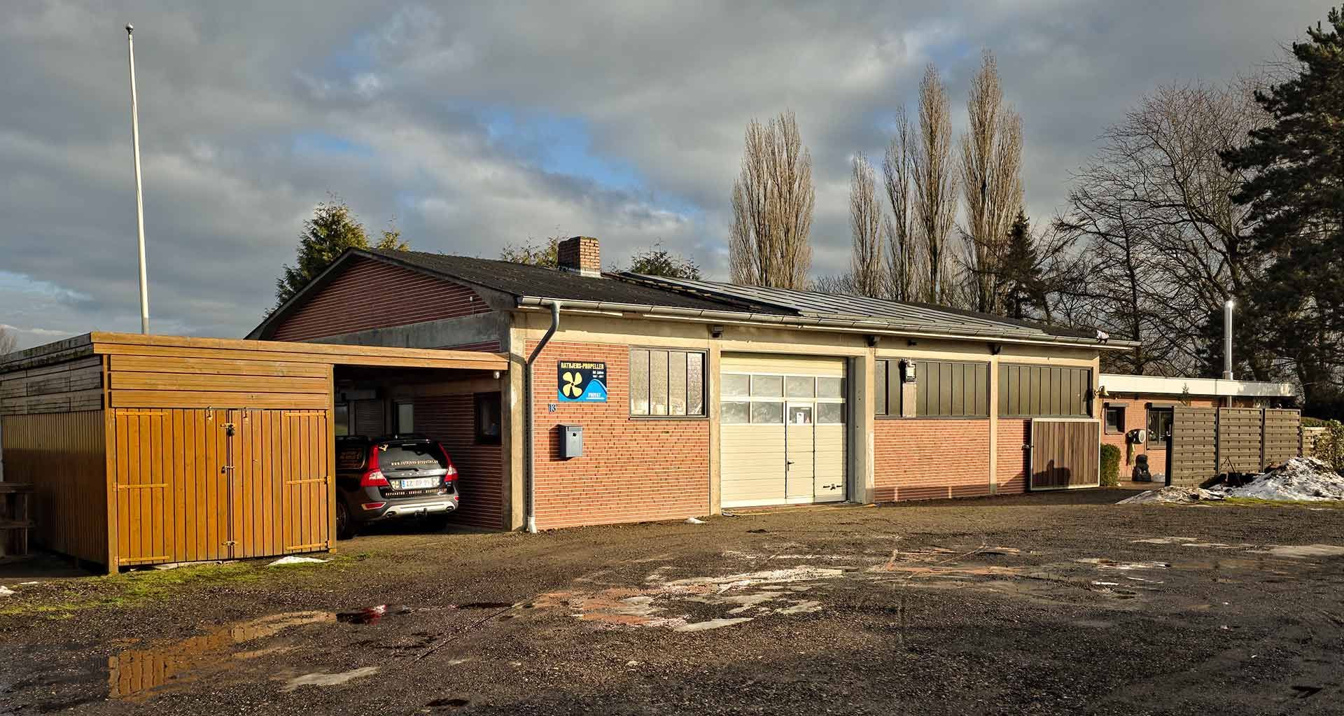 Holzgebäude mit braun-weiß gestreifter Fassade, Garagentor und Kiesauffahrt.