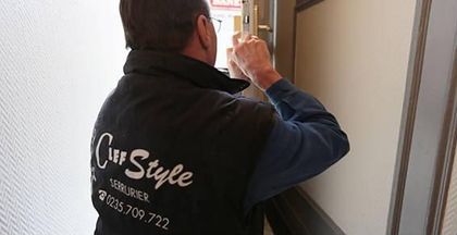 Un ouvrier en gilet noir applique de la peinture sur un mur près d’une porte