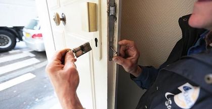 Deux personnes examinent une serrure de porte avec une clé, près d’une porte ouverte et d’une voiture garée à l’extérieur