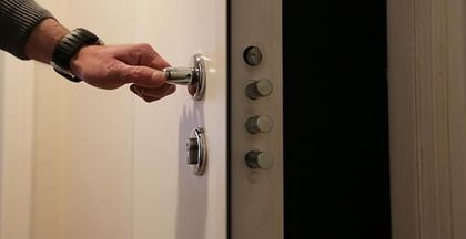 Une main tourne une poignée de porte argentée pour ouvrir une porte blanche