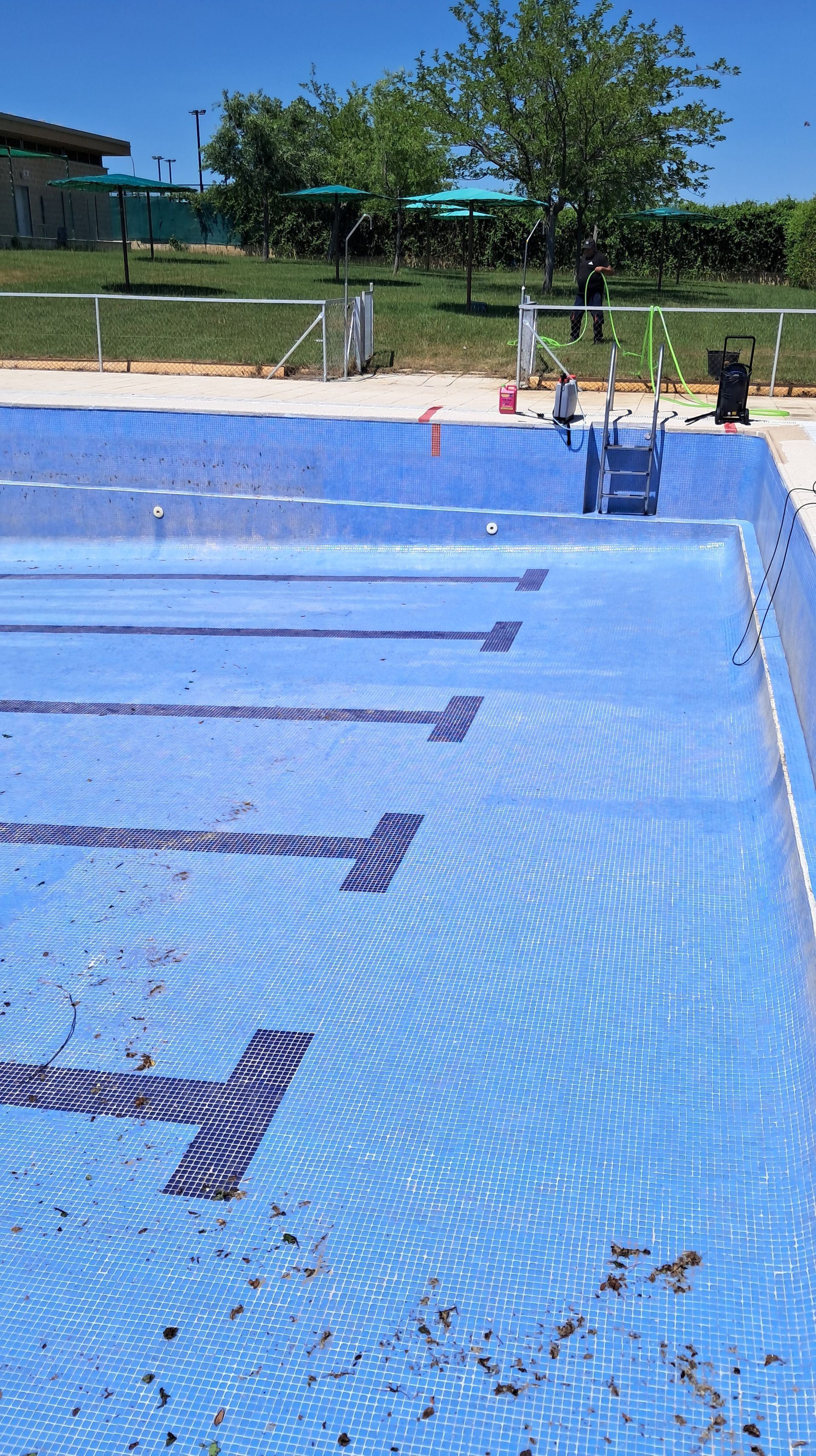 Piscina azul vacía con marcas de carril, bajo un cielo azul brillante.