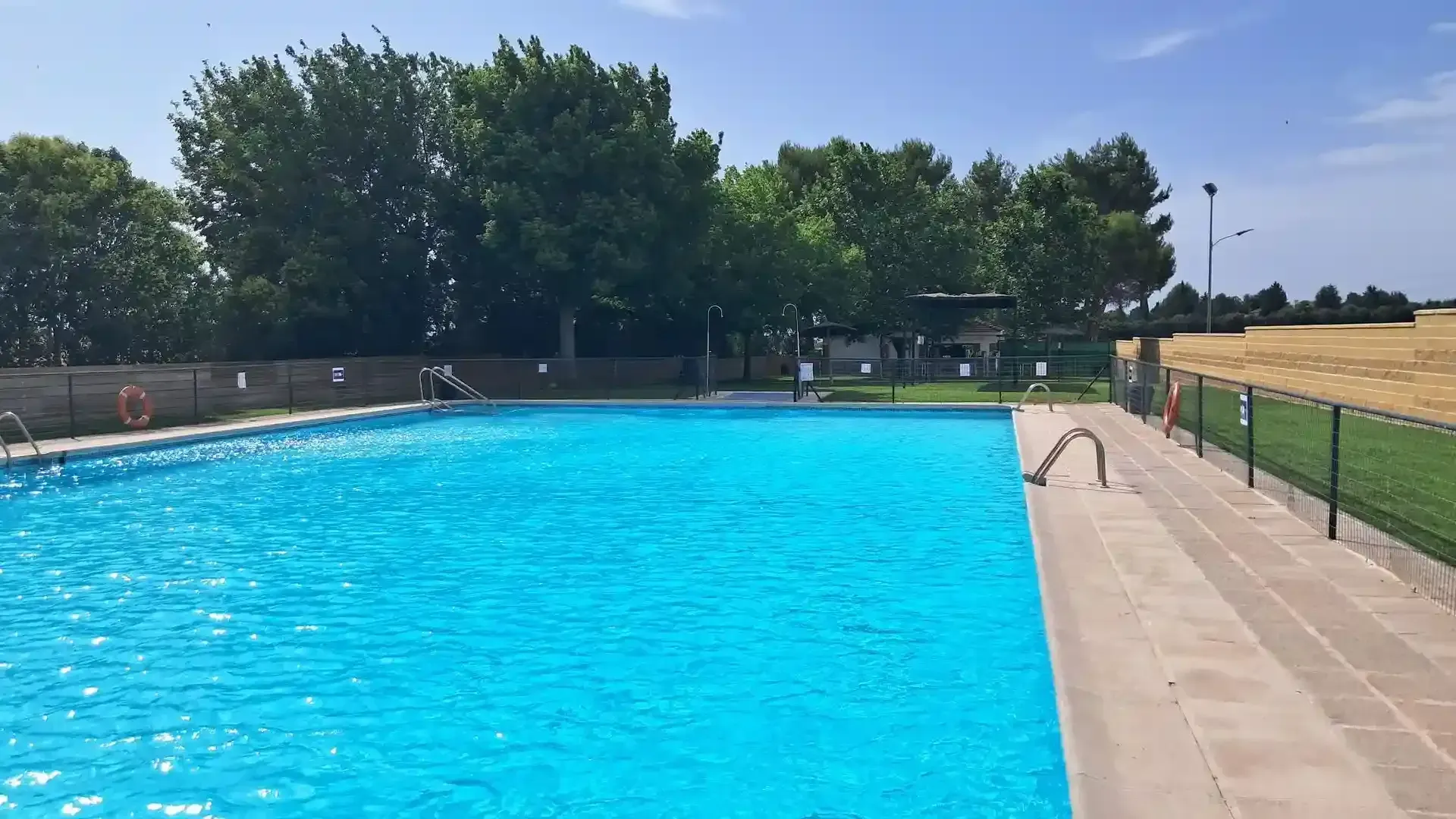 Piscina azul en un día soleado con árboles al fondo.